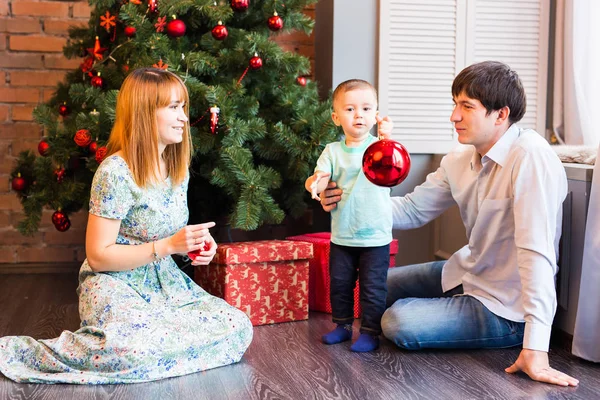 Familia, Navidad, x-mas, invierno, la felicidad y el concepto de la gente - sonriente familia con el niño sentado bajo el árbol de Navidad — Foto de Stock