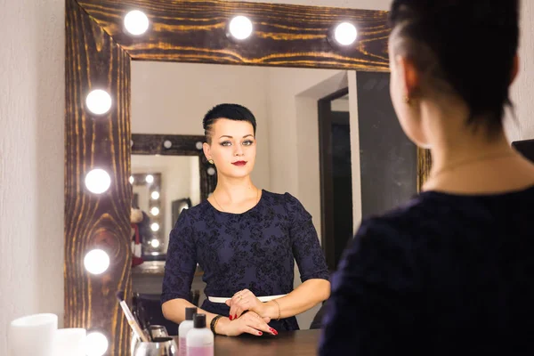 Hermosa chica con el pelo corto mirando a través del espejo en el vestidor — Foto de Stock