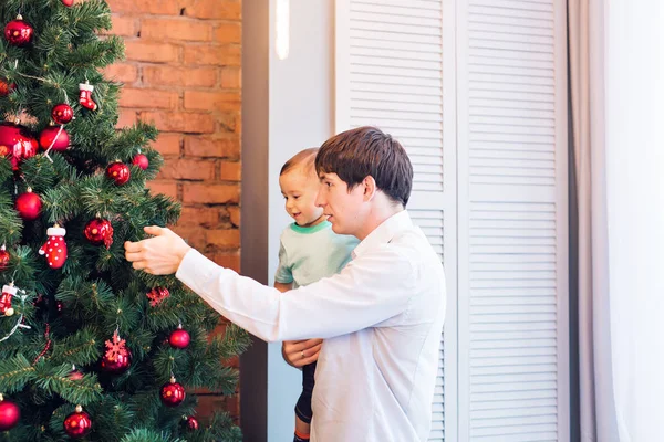 Pai feliz e seu filhinho decorando a árvore de Natal em casa . — Fotografia de Stock