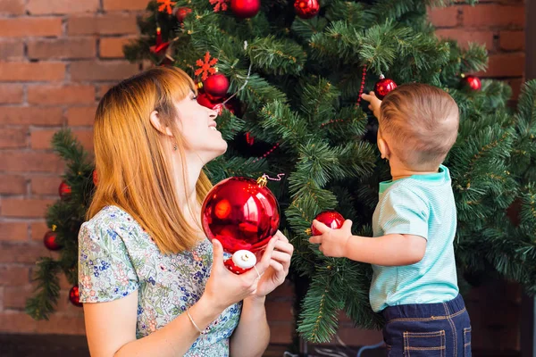 Mother helping little boy to decorate christmas tree at home