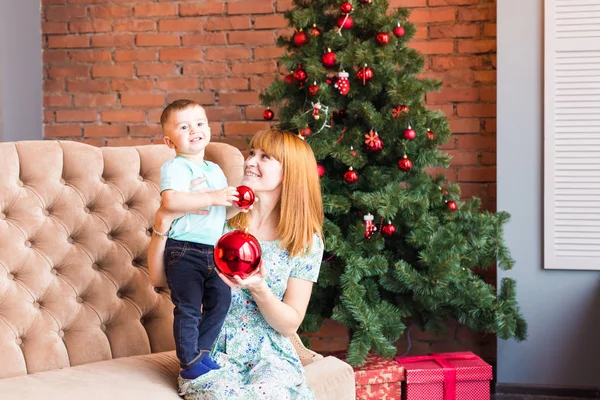 Πορτρέτο της ευτυχισμένη μητέρα και γέλιο μωρού εκμετάλλευση μπιχλιμπίδι εναντίον εγχώριο εσωτερικό εορταστική με Χριστουγεννιάτικο δέντρο. — Φωτογραφία Αρχείου