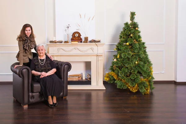 母亲和女儿的微笑、 立场和相机，拥抱彼此对圣诞树的姿势. — 图库照片