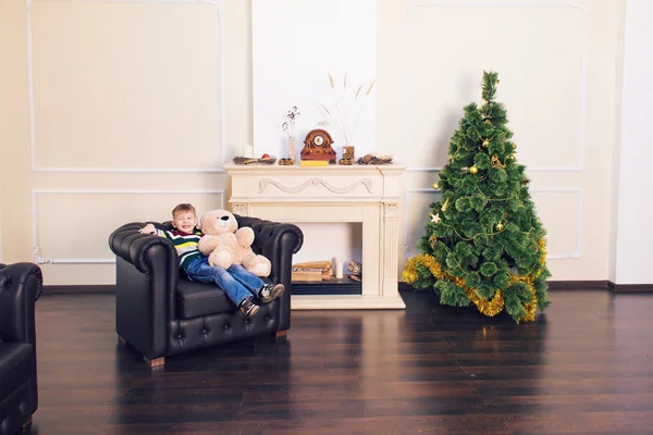 Menino brincando com urso de brinquedo macio perto da árvore de Natal . — Fotografia de Stock