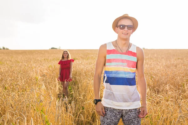 Schöner Kerl auf einem Feld und schönes Mädchen, das hinter steht — Stockfoto