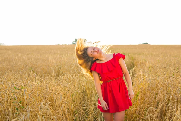 Hermosa chica romántica al aire libre. Hermosa modelo en vestido corto rojo en el campo. Cabello largo soplando en el viento. Retroiluminado, tonos cálidos de color —  Fotos de Stock