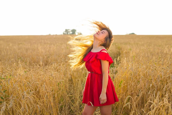 Hermosa chica romántica al aire libre. Hermosa modelo en vestido corto rojo en el campo. Cabello largo soplando en el viento. Retroiluminado, tonos cálidos de color —  Fotos de Stock