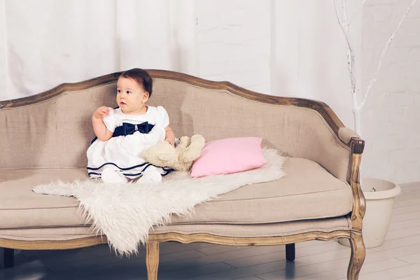 Счастливая маленькая девочка сидит на диване с игрушкой плюшевого мишки . — стоковое фото