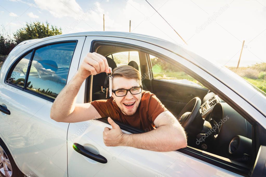 Attractive young happy man showing his new car keys and laughing