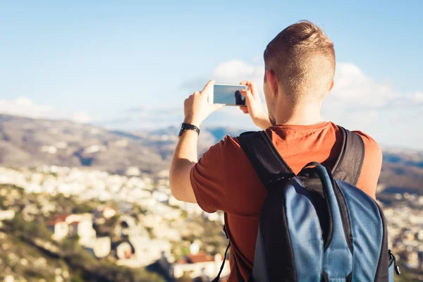 Arkadan bir genç adam turist görünüşü ile smartphone ile manzara fotoğrafı çekmek sırt çantası — Stok fotoğraf