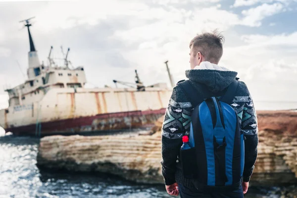 Turista masculino mirando a un barco abandonado en el mar o vista trasera al mar. Concepto aventura y turismo . — Foto de Stock