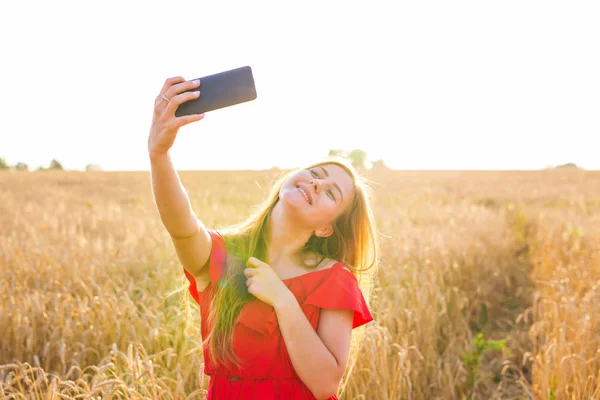 Technologie, zomer vakantie, vakantie en mensen concept - jonge vrouw nemen selfie glimlachen door smartphone op granen veld — Stockfoto