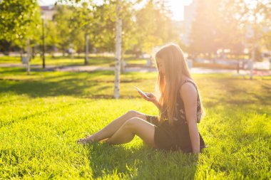 yaşam tarzı, yaz, tatil, teknoloji ve insan kavramı ile smartphone çim parkta oturan genç kız gülümseyerek-