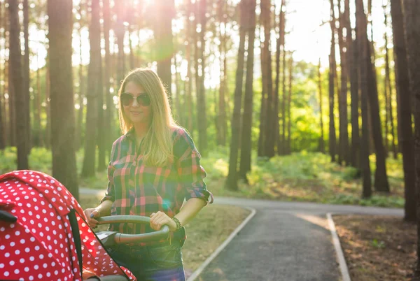 Мать с ребенком в детской коляске прогулка в летнем парке — стоковое фото