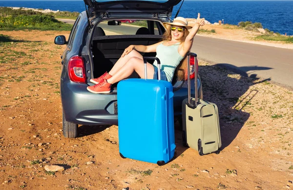 Cestování, letní prázdniny a dovolené koncepce - mladá žena s kufry na cestě autem. Ona sedí v autě zpět a gesto palce nahoru. — Stock fotografie