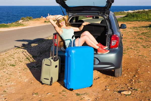 Reise, Sommerferien und Urlaubskonzept - junge Frau mit Koffer auf Autofahrt. Sie sitzt hinten im Auto und gestikuliert mit dem Daumen nach oben. — Stockfoto