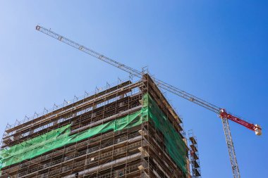 Mavi gökyüzüne karşı inşaat halindeki vinç ve bina