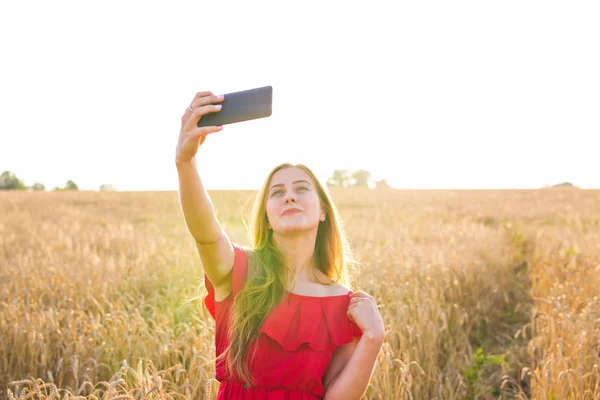 Technologie, zomer vakantie, vakantie en mensen concept - jonge vrouw nemen selfie glimlachen door smartphone op granen veld. — Stockfoto