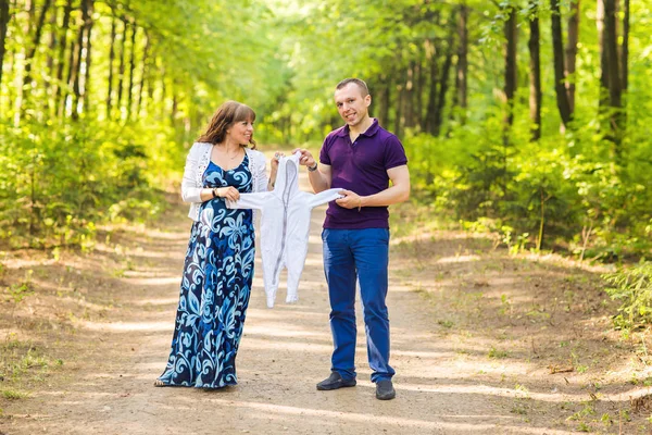 Porträt einer kaukasischen Schwangeren und ihres Mannes, die Kleidung für Babys im Freien tragen — Stockfoto