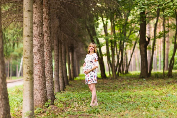 Mulher grávida bonita toca sua barriga no parque — Fotografia de Stock