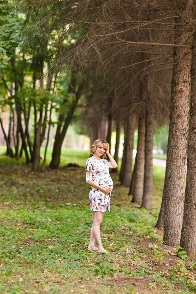 Beautiful pregnant woman touches her belly in the park — Stock Photo, Image