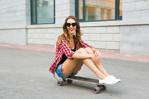 Νεαρή γυναίκα που κάθεται στο σκέιτερ. Χαμογελαστό γυναίκα με skateboard σε εξωτερικούς χώρους — Φωτογραφία Αρχείου
