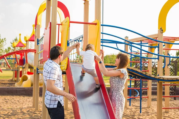 Verano, infancia, ocio y concepto familiar - niño feliz y sus padres en los niños parque infantil escalada marco — Foto de Stock