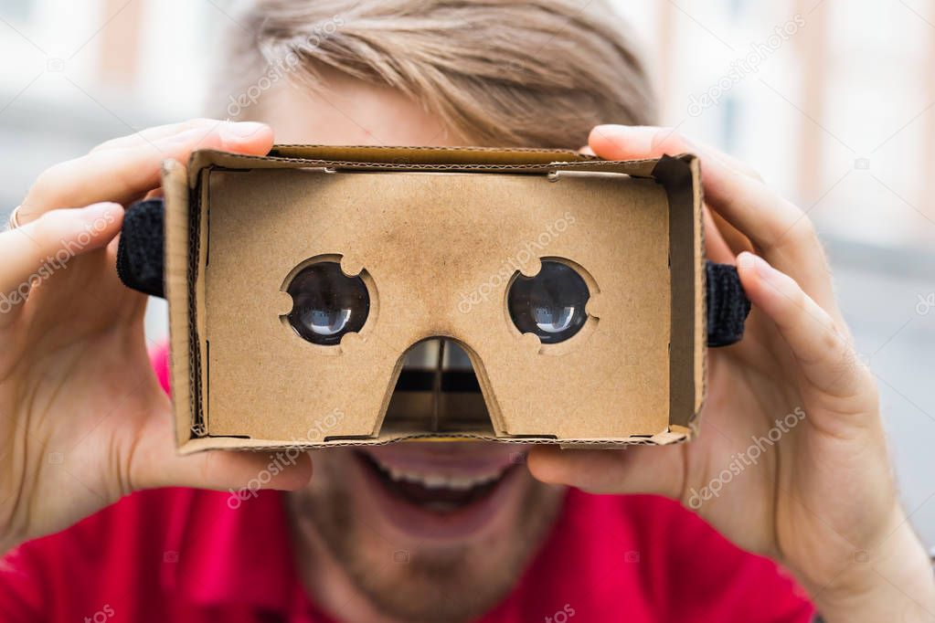 Funny man using cardboard virtual reality goggle outdoors
