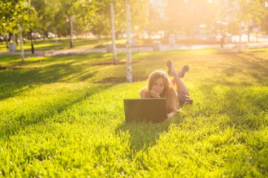 Bahar zaman parkta yeşil çimenlerin üzerinde dizüstü bilgisayar ile bir güzel öğrenci kız portresi.