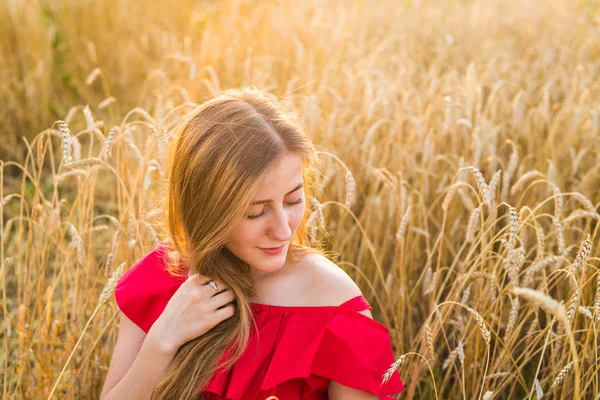 Portret van een jonge vrouw in rode jurk op een achtergrond van gouden haver veld, zomer buiten. — Stockfoto