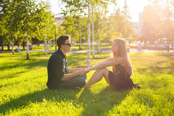 Концепция дружбы и любви с молодой парой, сидящей на траве и разговаривающей . — стоковое фото