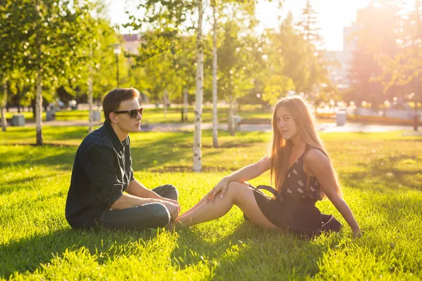 Концепция дружбы и любви с молодой парой, сидящей на траве и разговаривающей . — стоковое фото