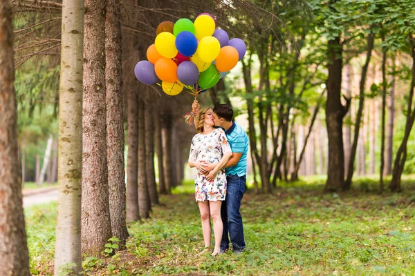 Jovem casal homem e sua esposa grávida com balões ao ar livre — Fotografia de Stock