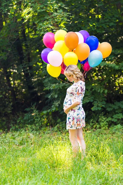 Young pregnant woman holding colorful balloons outdoors — Stock Photo, Image