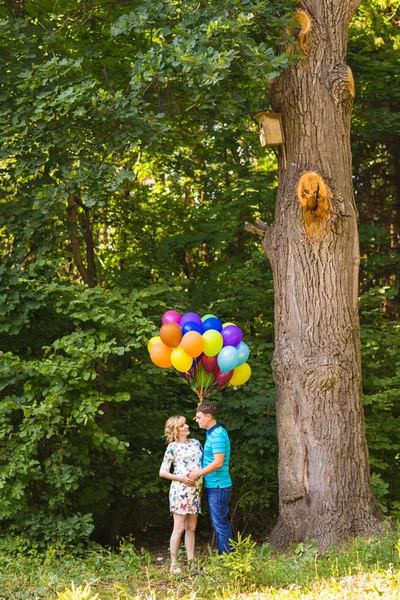 Joven pareja hombre y su embarazada esposa con globos al aire libre — Foto de Stock
