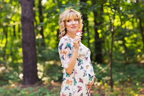 Outdoor portrait of young pregnant woman holding a lollipop in summer nature — Stock Photo, Image