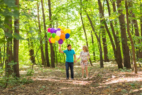 Jovem casal homem e sua esposa grávida com balões ao ar livre — Fotografia de Stock