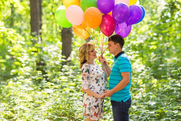 Jovem casal homem e sua esposa grávida com balões ao ar livre — Fotografia de Stock