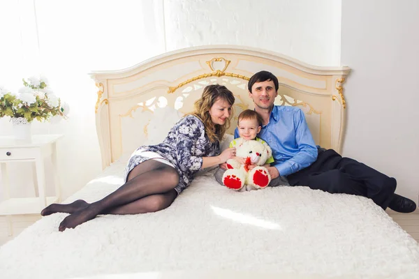 Aile, ebeveyn ve çocuk kavramı - mutlu anne, baba ve oğul yatakta evde yatak odasında oyuncak ayı ile birlikte oynarken. — Stok fotoğraf