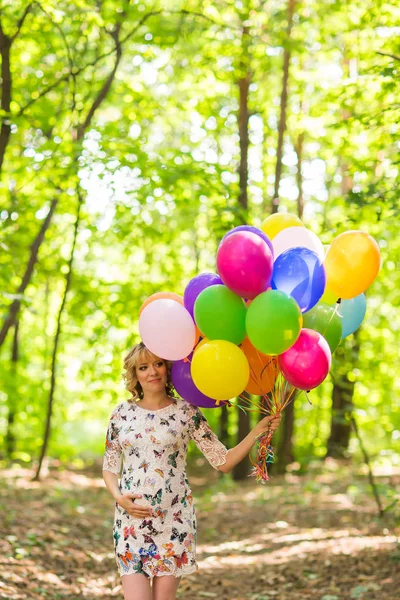Young pregnant woman holding colorful balloons outdoors Stock Image