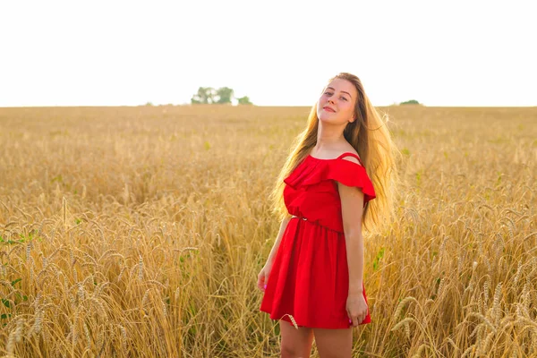 Hermosa chica romántica al aire libre. Hermosa modelo en vestido corto rojo en el campo. Cabello largo soplando en el viento. Retroiluminado, tonos cálidos de color —  Fotos de Stock