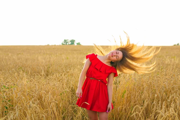 Hermosa chica romántica al aire libre. Hermosa modelo en vestido corto rojo en el campo. Cabello largo soplando en el viento. Retroiluminado, tonos cálidos de color — Foto de Stock