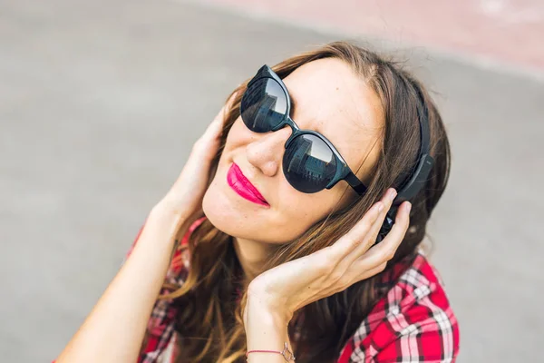 リラックスして、通りでヘッドフォンで音楽を聴く若い笑顔の女性. — ストック写真