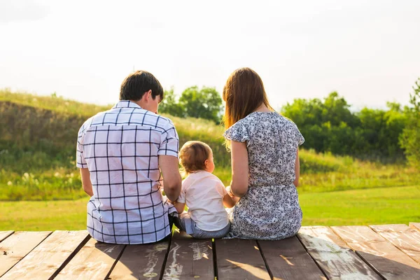 Fin de semana, niños y el concepto de paternidad - Familia sentada en la superficie de madera y mirando a la hermosa vista de verano — Foto de Stock