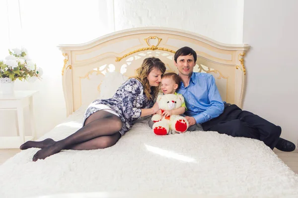 Conceito de família, paternidade e filhos - Mãe feliz, pai e filho brincando juntos com ursinho de pelúcia na cama no quarto em casa . — Fotografia de Stock