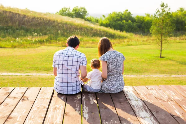 Retrato familiar. Imagen de feliz padre amoroso, madre y su bebé al aire libre. Papá, mamá y el niño contra Green Hill. Vista trasera . — Foto de Stock