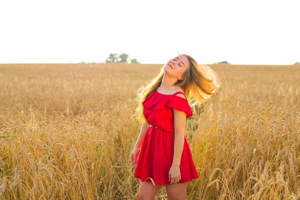 Hermosa chica romántica al aire libre. Hermosa modelo en vestido corto rojo en el campo. Cabello largo soplando en el viento. Retroiluminado, tonos cálidos de color . — Foto de Stock
