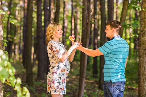 Grossesse, famille, bonheur et concept amusant - Homme et femme enceinte s'amusent avec des bonbons dans le parc — Photo