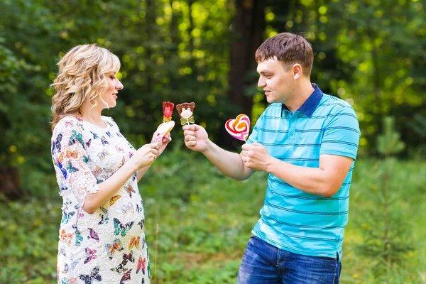 Gravidez, família, felicidade e diversão conceito - Homem e mulher grávida se divertir com doces no parque — Fotografia de Stock
