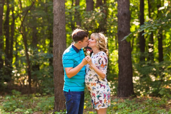 Těhotenství, Rodina, štěstí a zábavný koncept - Man a těhotná žena bavit s candy v parku — Stock fotografie