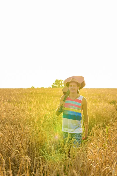 Junger Mann mit Gitarre auf dem Feld bei Sonnenuntergang — Stockfoto